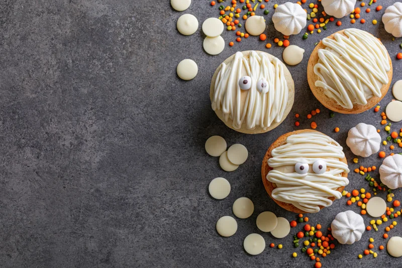 Halloween mummy cupcakes decorated with white icing and sprinkles on gray surface