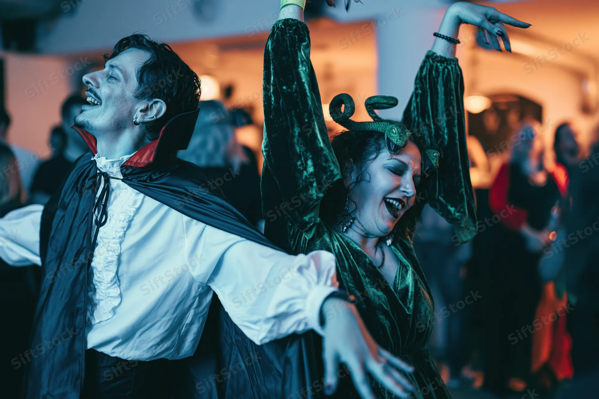 Man in vampire costume and woman in witch costume dancing together at a halloween party