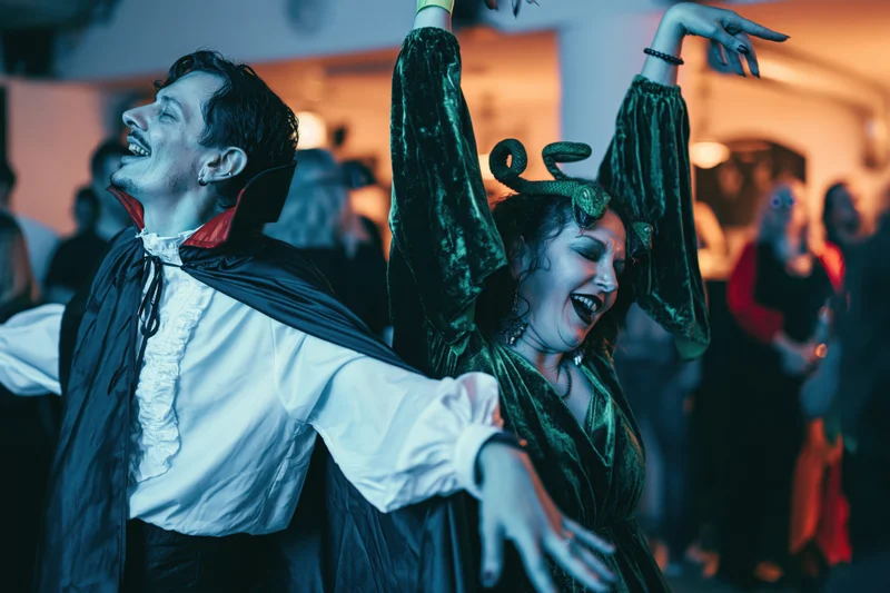 Man in vampire costume and woman in witch costume dancing together at a halloween party