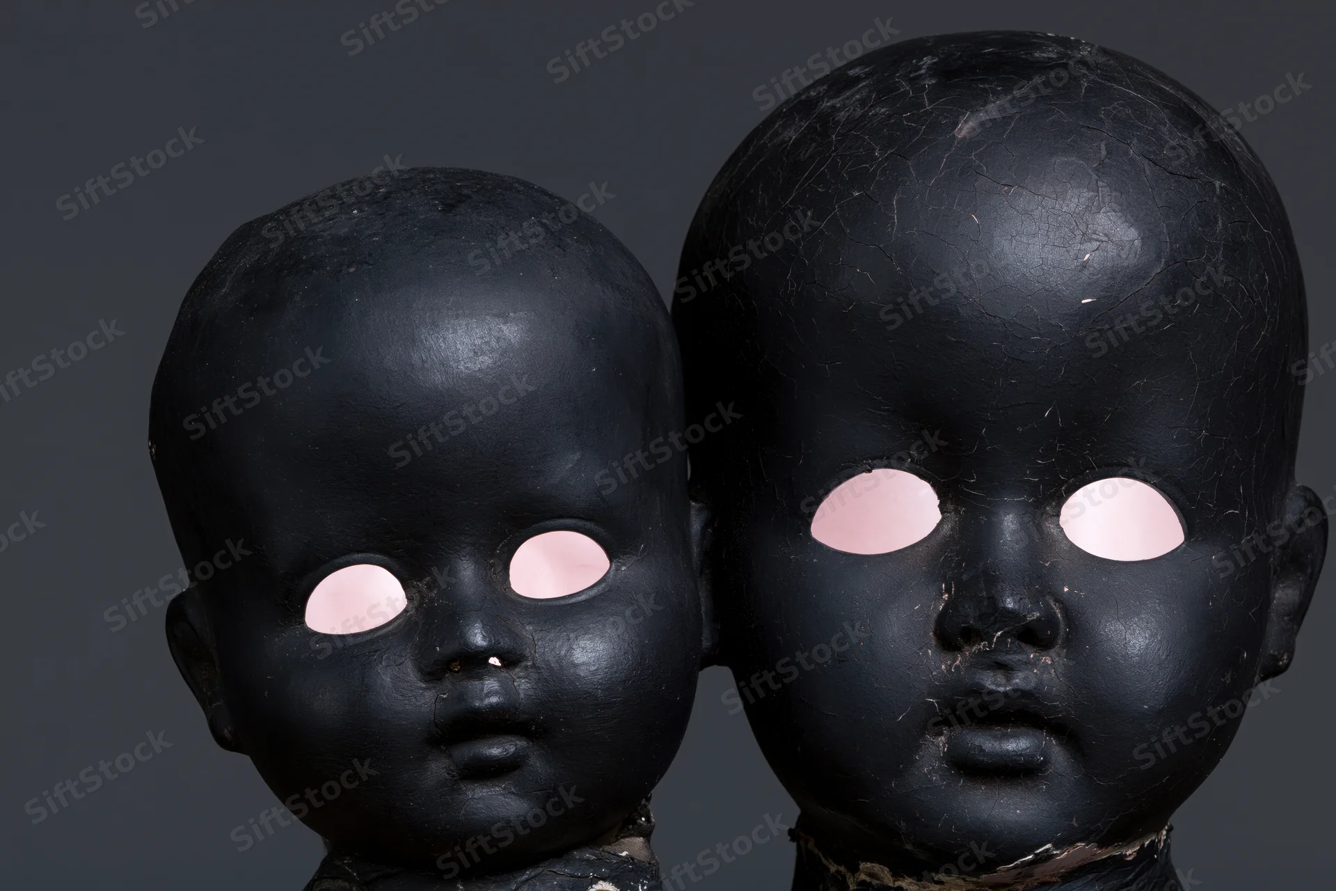 Two black-painted antique doll heads side by side, one smaller, against dark background