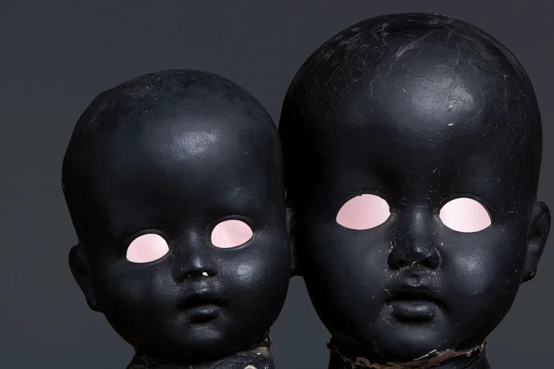 Two black-painted antique doll heads side by side, one smaller, against dark background