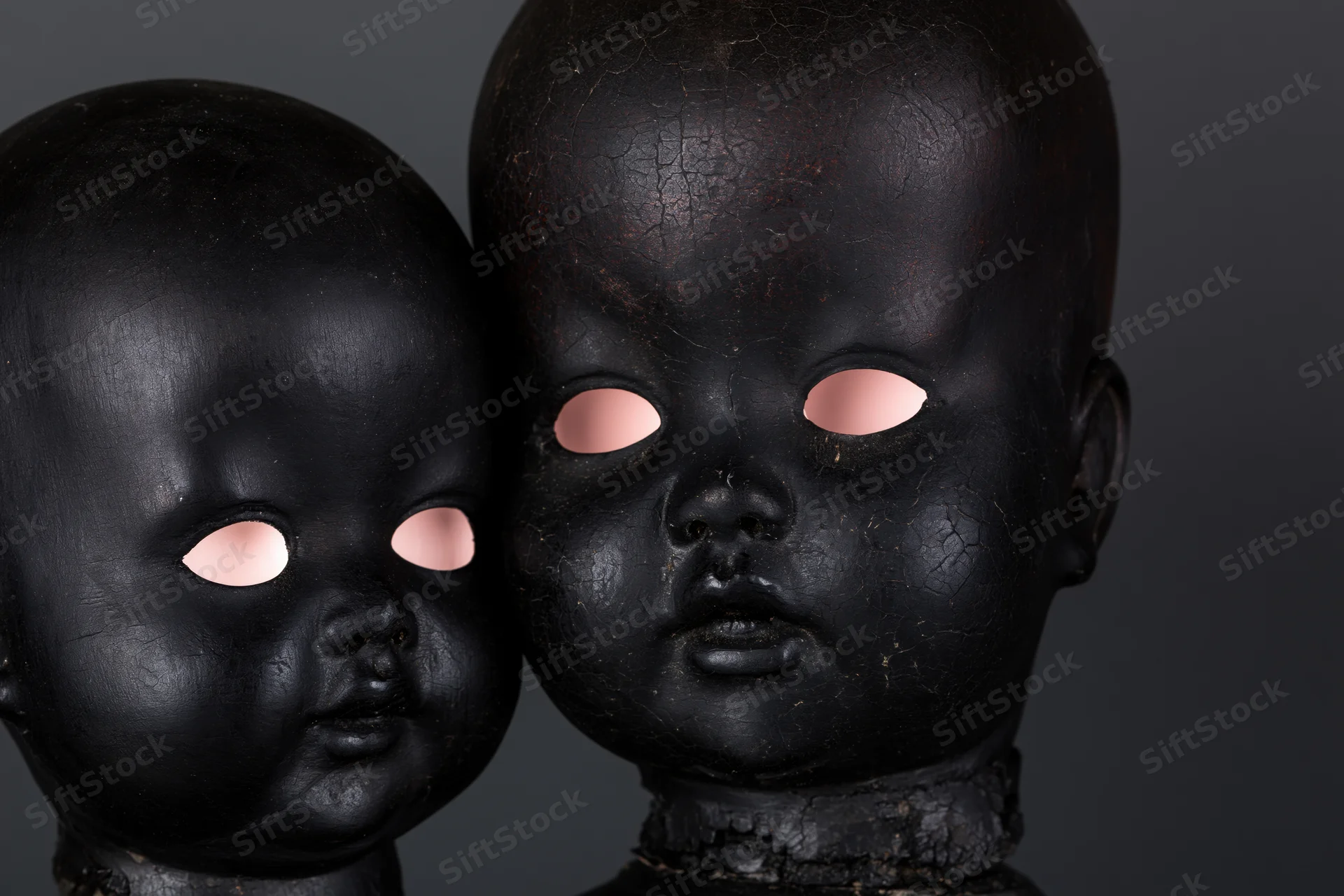 Two black-painted antique doll heads side by side, one smaller, against dark background