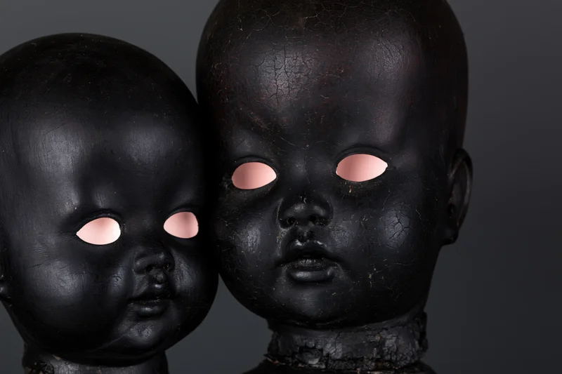 Two black-painted antique doll heads side by side, one smaller, against dark background