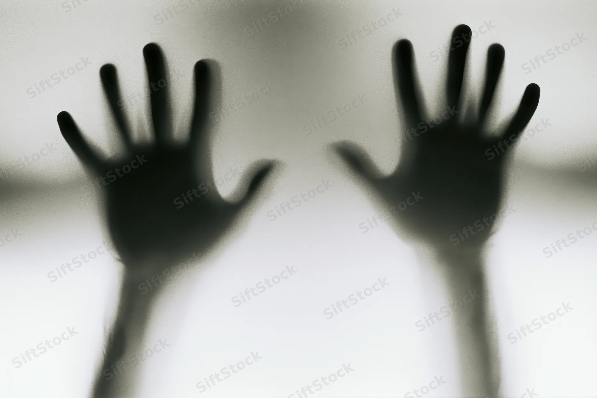 Blurred hands pressed against frosted glass in a shadowy silhouette