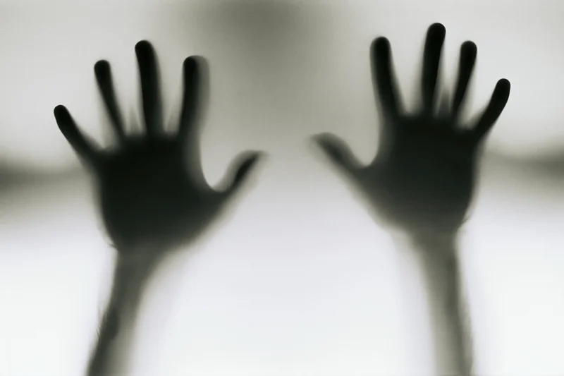Blurred hands pressed against frosted glass in a shadowy silhouette