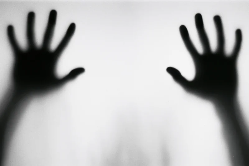 Blurred hands pressed against frosted glass in a monochrome horror scene