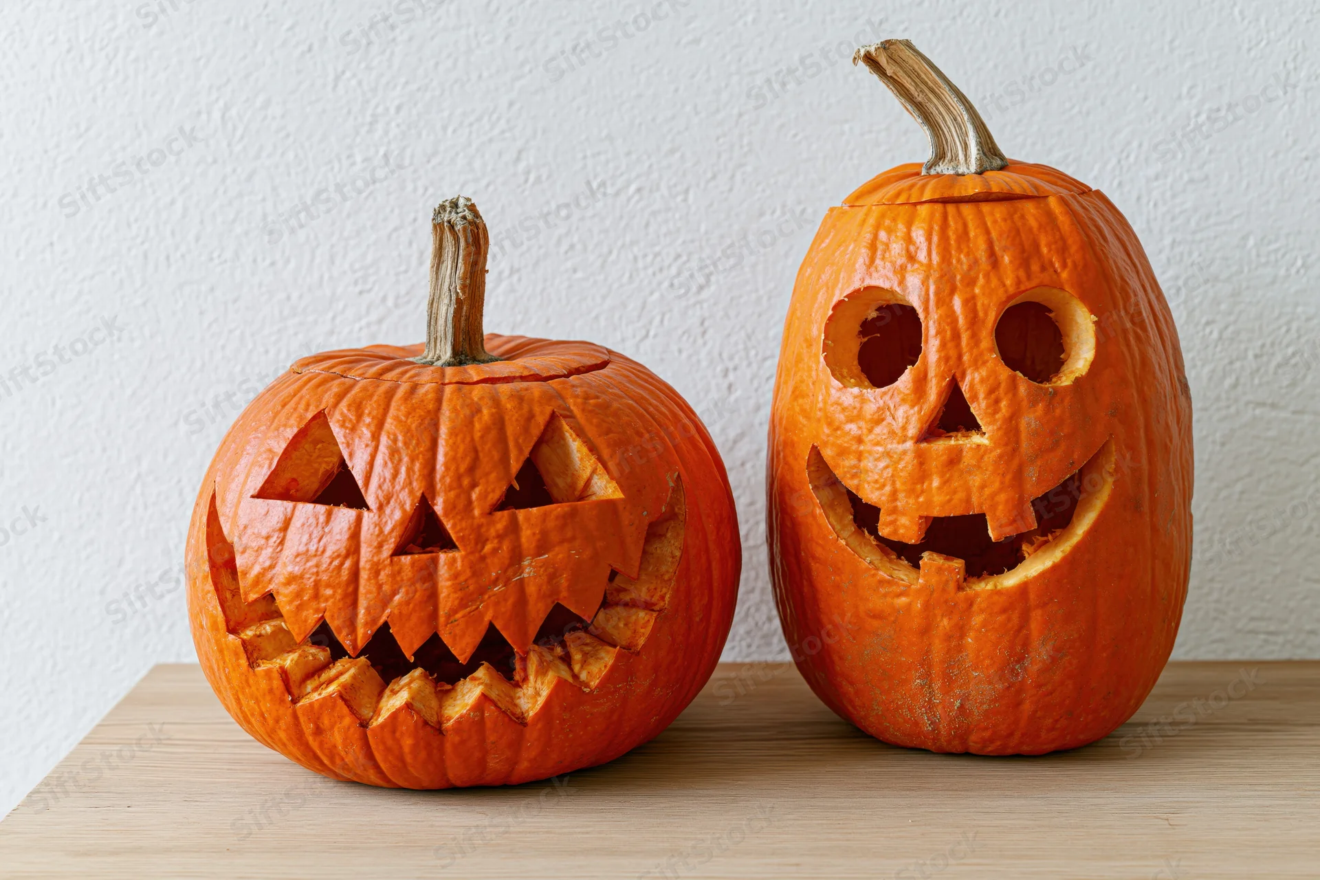 Two carved pumpkins with jack-o-lantern faces sitting side by side on a wooden table