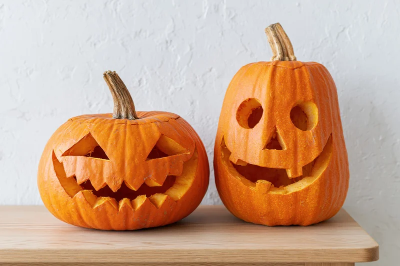 Two carved pumpkins with jack-o-lantern faces sitting side by side on a wooden table