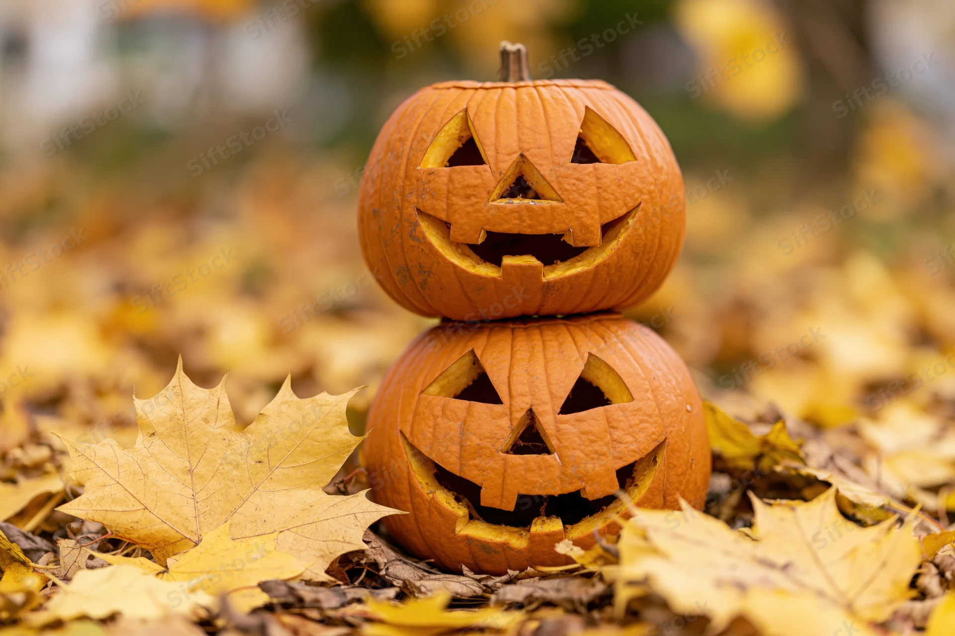 Two carved jack-o-lanterns stacked on autumn leaves outdoors