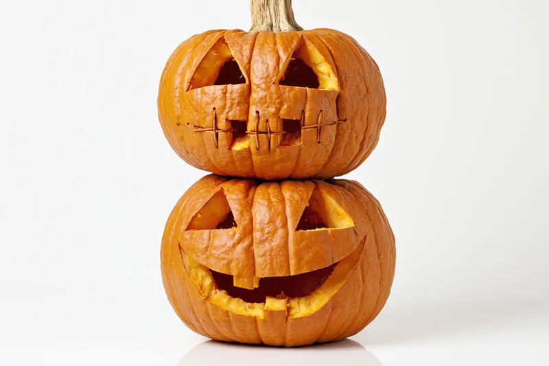 Two carved jack-o-lanterns stacked vertically on a white surface