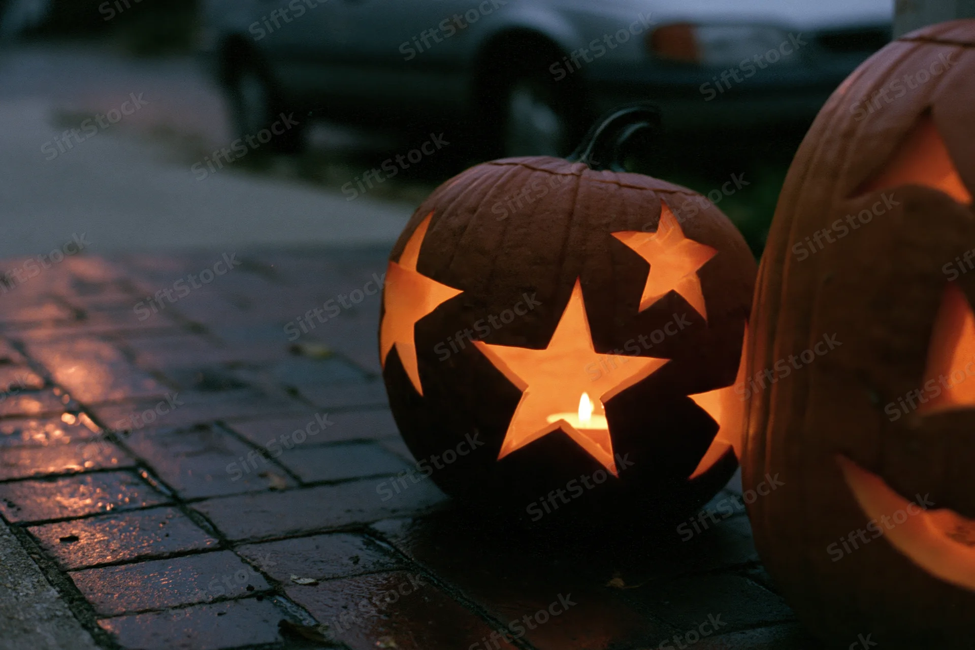Carved pumpkins with star cutouts glowing on wet brick pavement at night