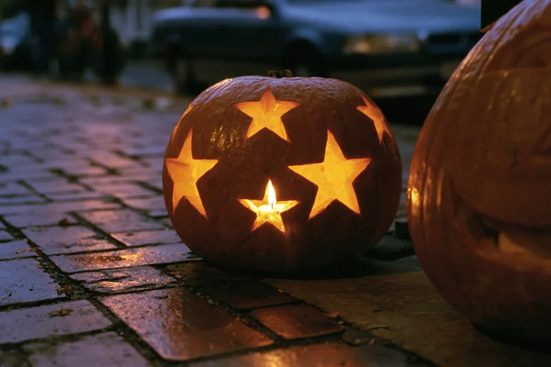 Carved pumpkin with star cutouts glowing on wet brick pavement at night