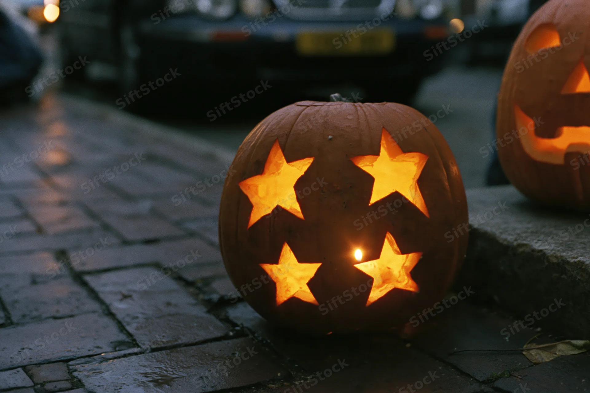 Carved pumpkin with star cutouts glowing on wet brick pavement at night