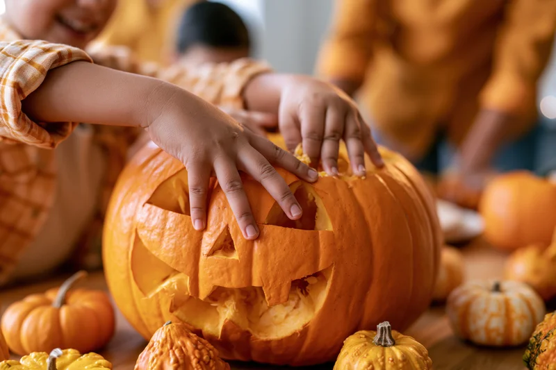 Children's hands reaching into a carved jack-o-lantern on a wooden table surrounded by small pumpkins