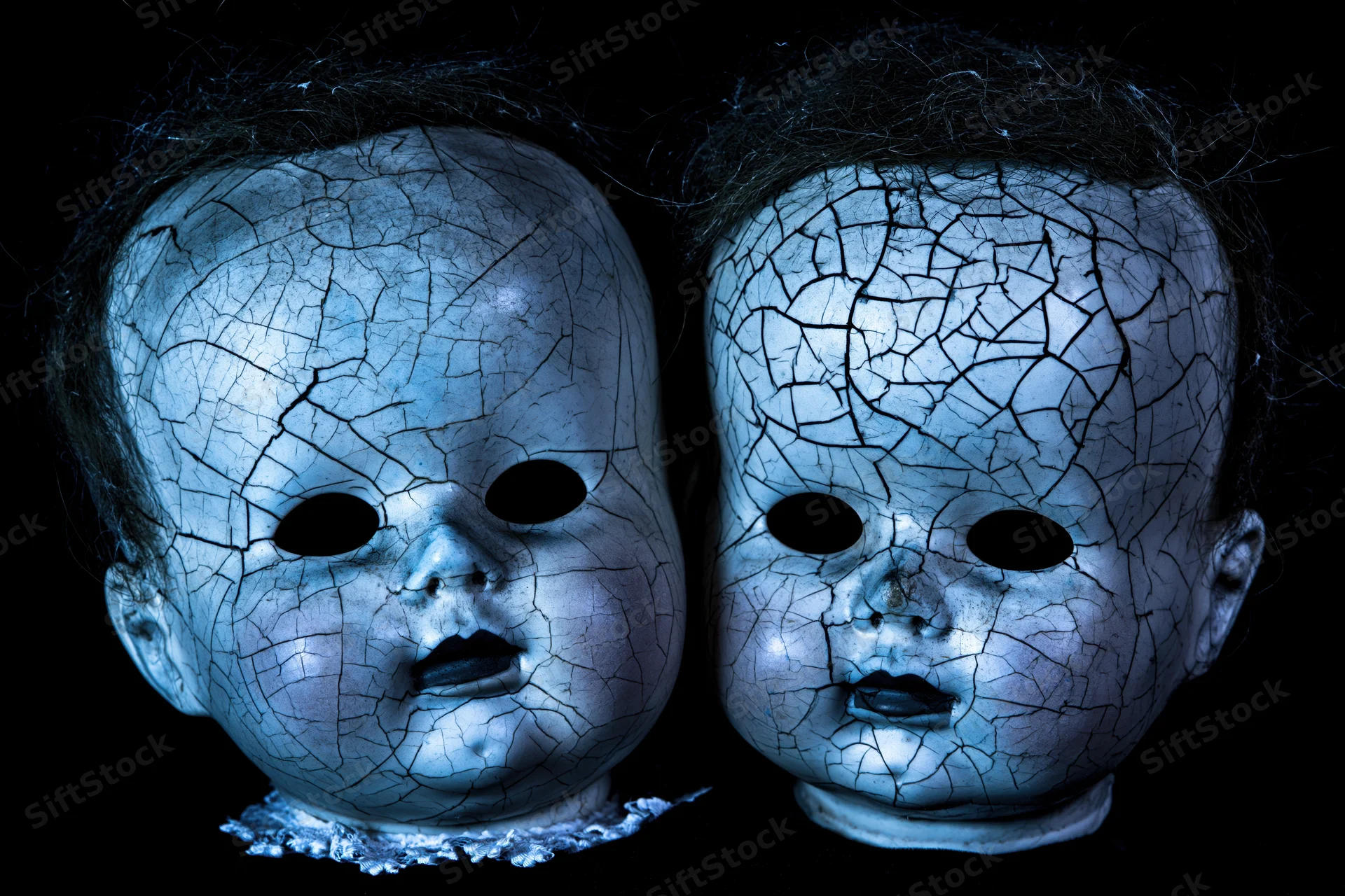 Two cracked vintage baby doll heads side by side against black background