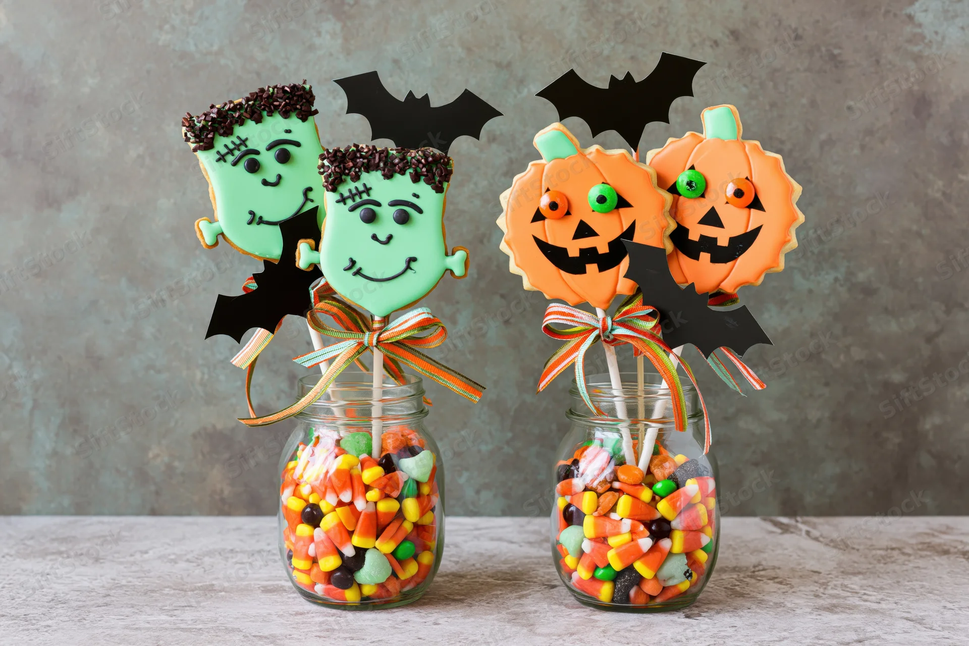 Halloween-themed cookies on sticks arranged in glass jars filled with candy corn and mixed sweets on a table