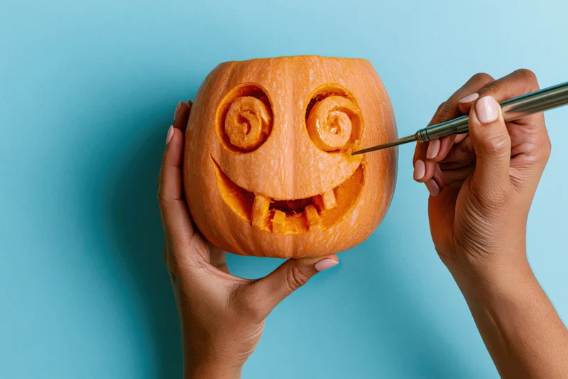 Hands carving a butternut squash jack-o-lantern against a blue background