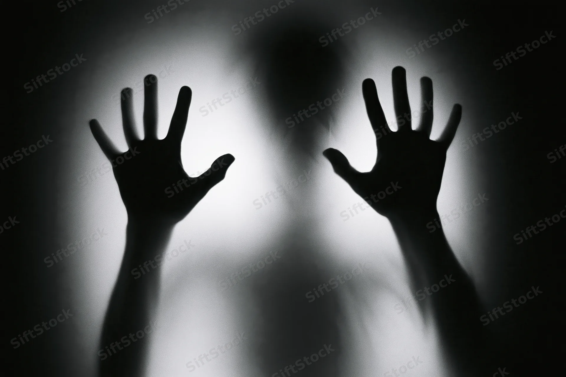 Silhouette of hands pressing flat against frosted glass with blurred figure behind