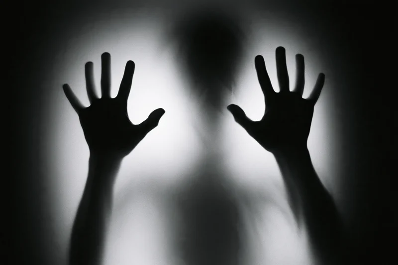 Silhouette of hands pressing flat against frosted glass with blurred figure behind