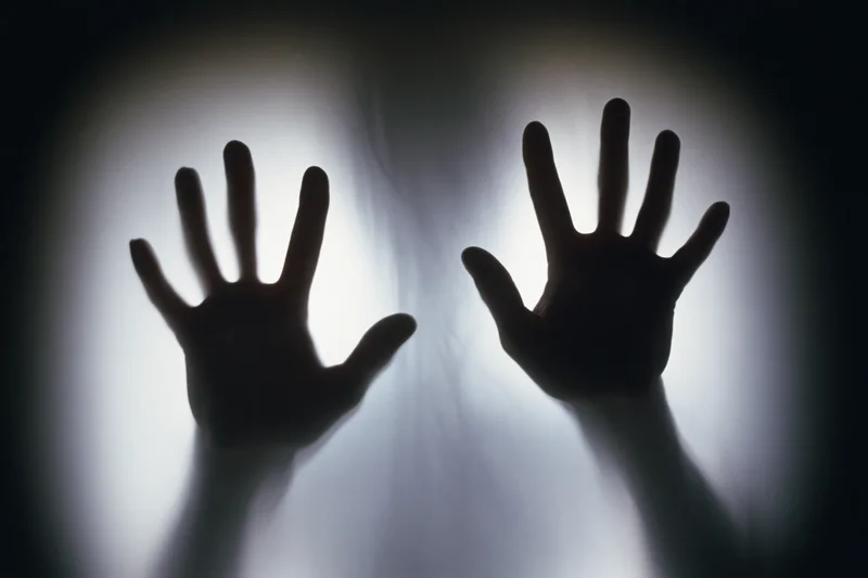Silhouetted hands pressing flat against frosted glass panel in dark interior