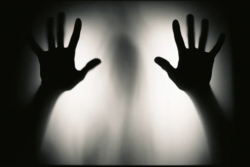 Silhouetted hands pressed against frosted glass in a darkened space