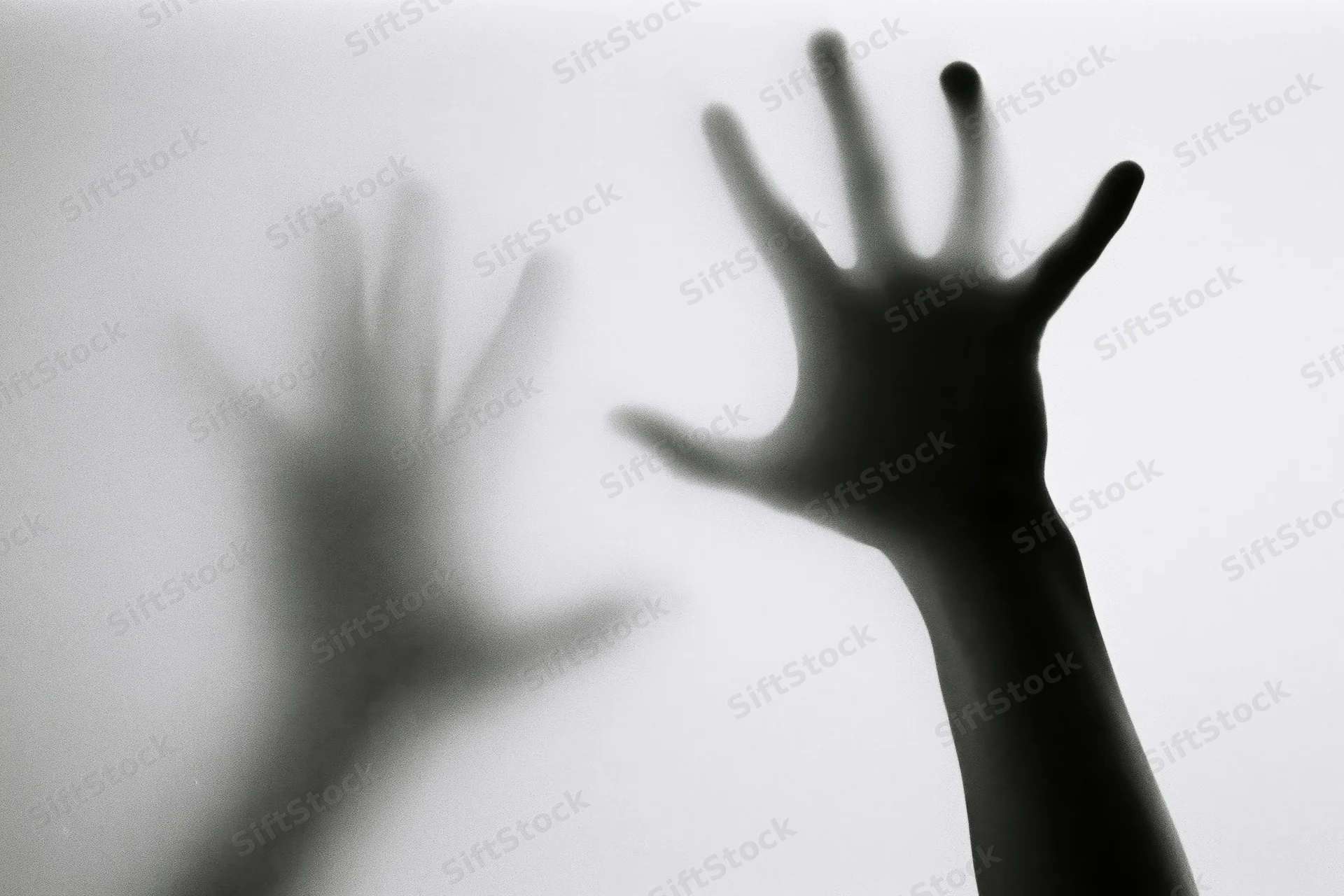 Hands pressing against a fogged translucent surface in silhouette