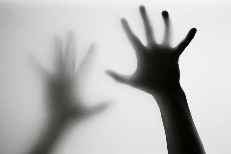Hands pressing against a fogged translucent surface in silhouette
