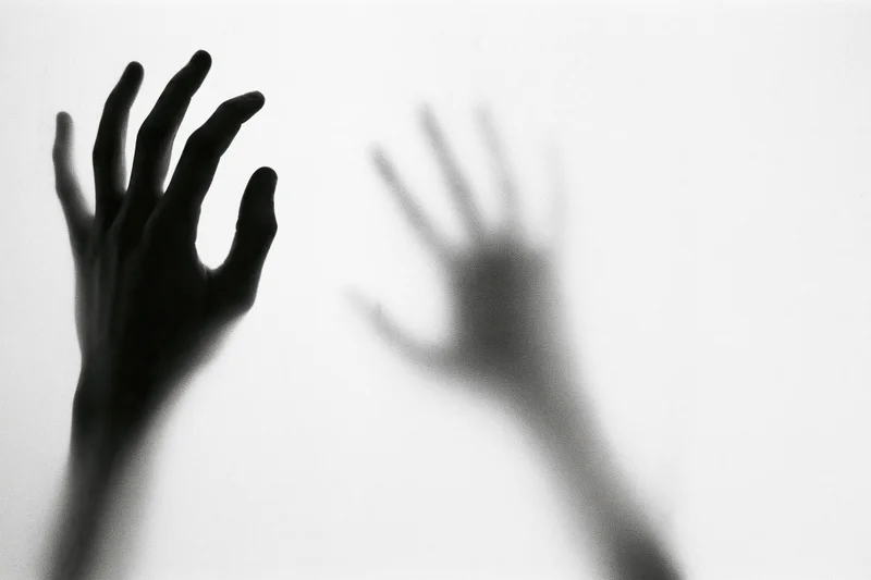 Hands pressing against translucent glass with one in sharp focus and the other blurred in reflection