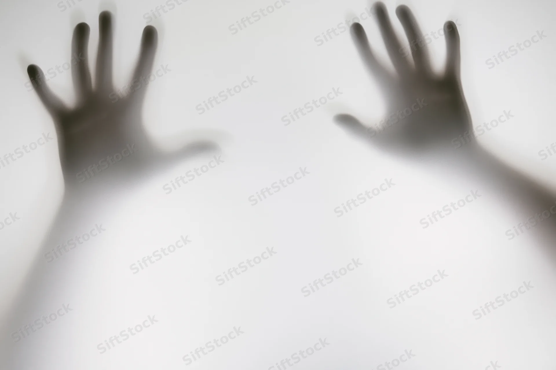 Two hands pressed against frosted glass with blurred shadows and soft light