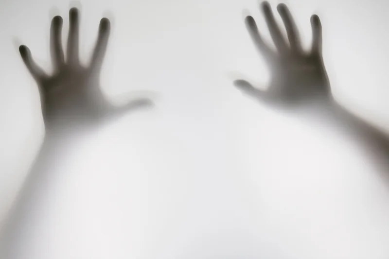 Two hands pressed against frosted glass with blurred shadows and soft light