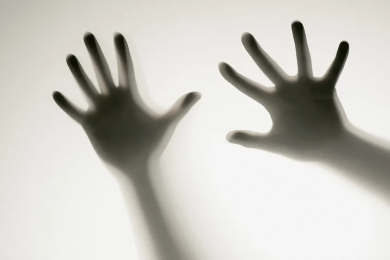 Two hands pressed against frosted glass in silhouette