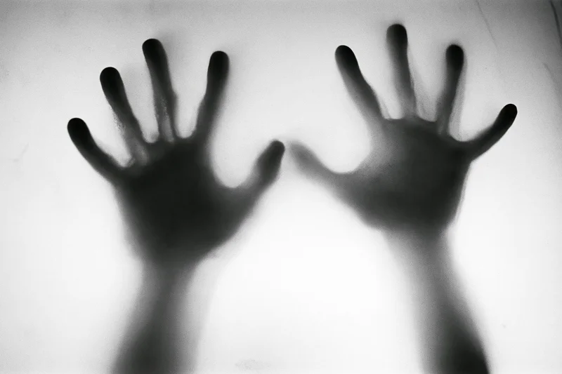 Two hands pressed flat against frosted glass with blurred silhouette effect