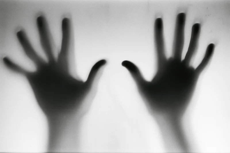 Two hands pressed flat against frosted glass in silhouette
