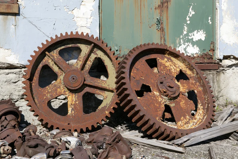 Two large rusted industrial gear wheels leaning against a weathered wall in a scrapyard