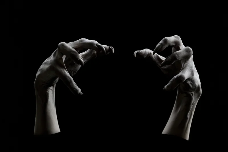 Two pale clawed hands reaching forward from darkness against black background