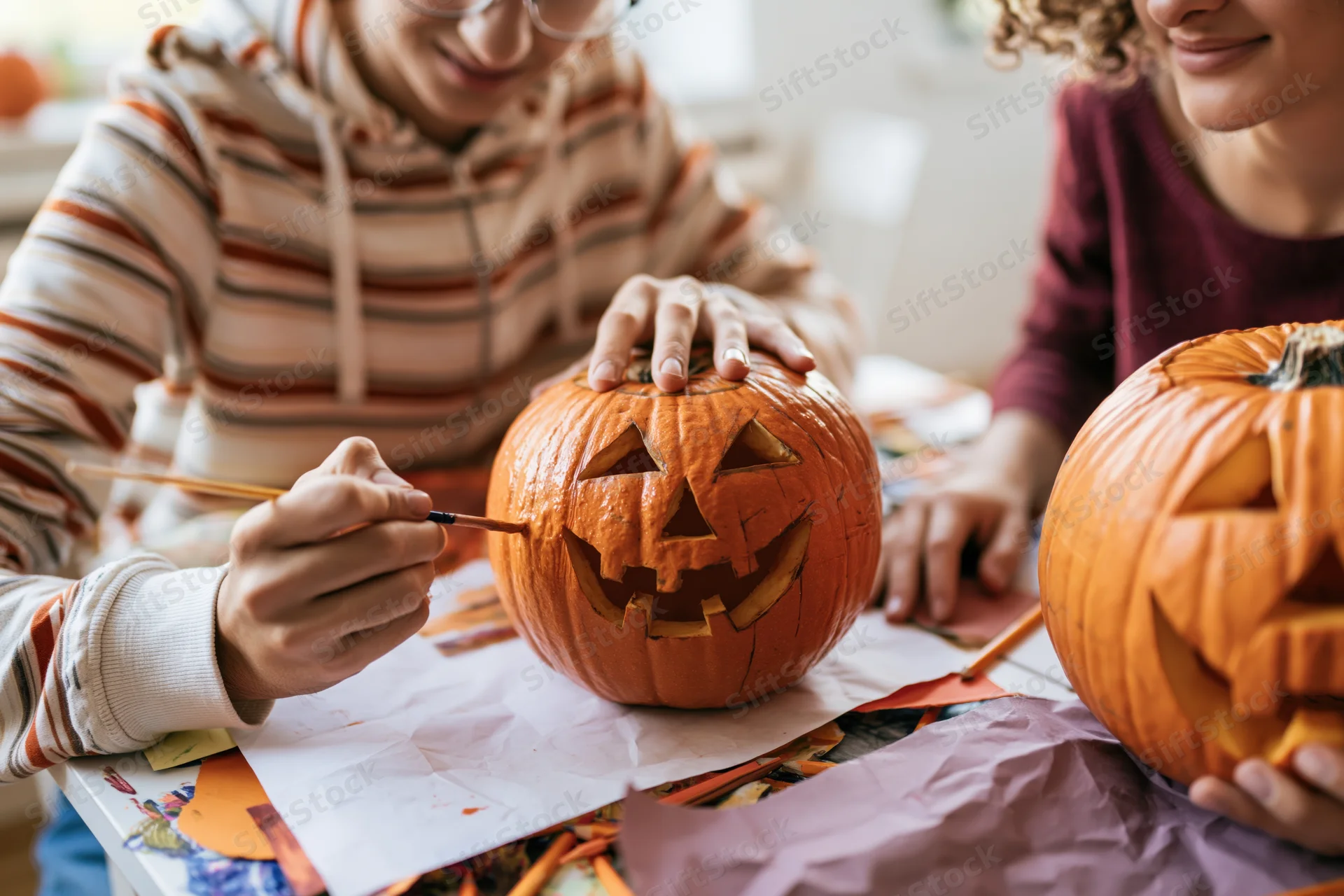 Two people carving pumpkins at a table with craft supplies for halloween