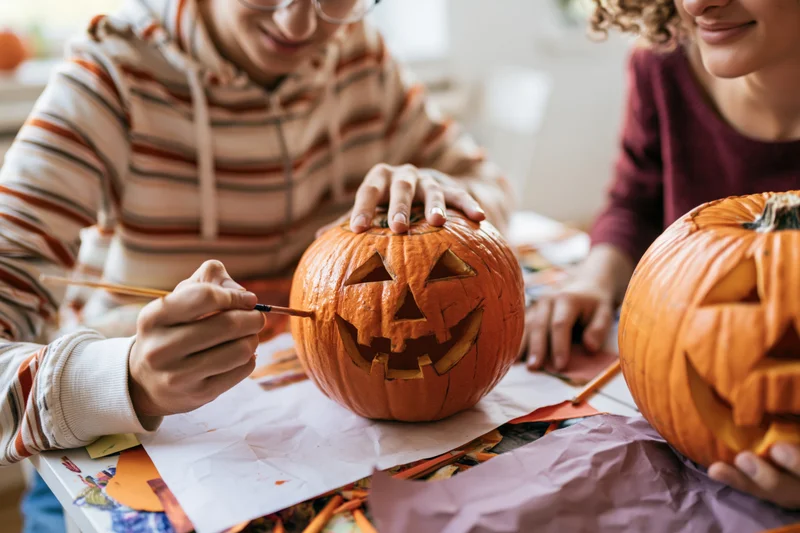 Two people carving pumpkins at a table with craft supplies for halloween