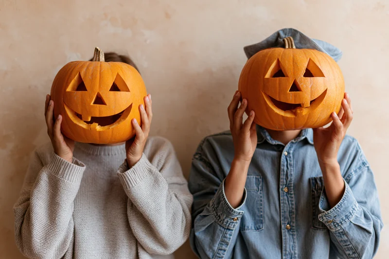 Two children holding carved pumpkins in front of their faces indoors