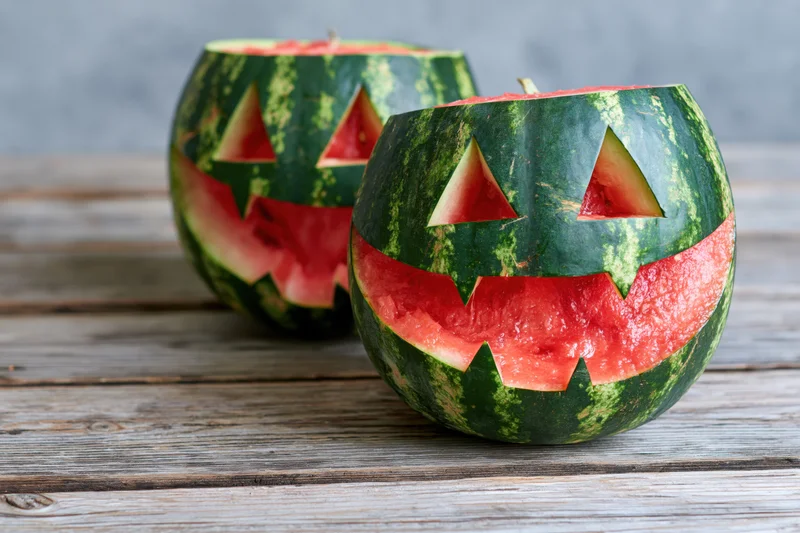 Two carved watermelons with jack-o-lantern faces on a wooden table