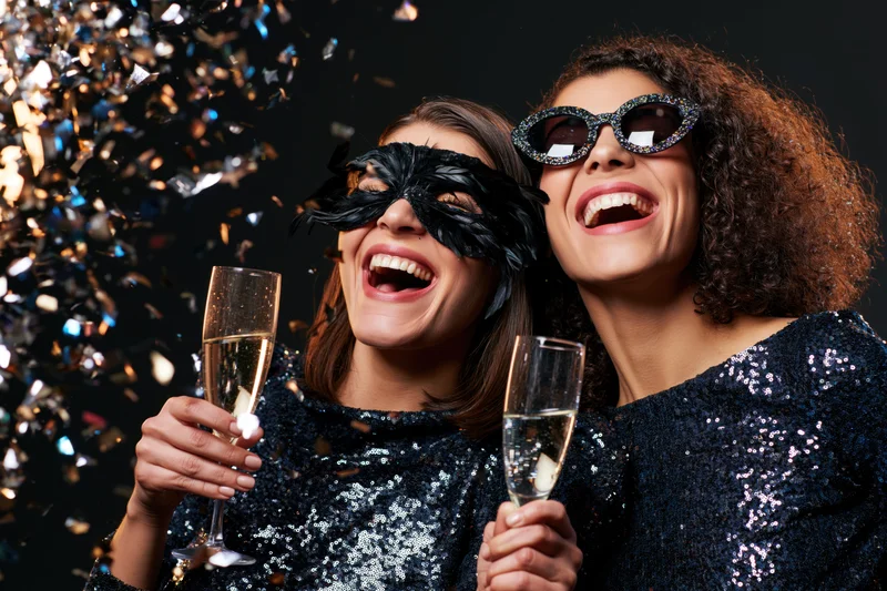 Two women laughing and toasting with champagne at a masquerade party