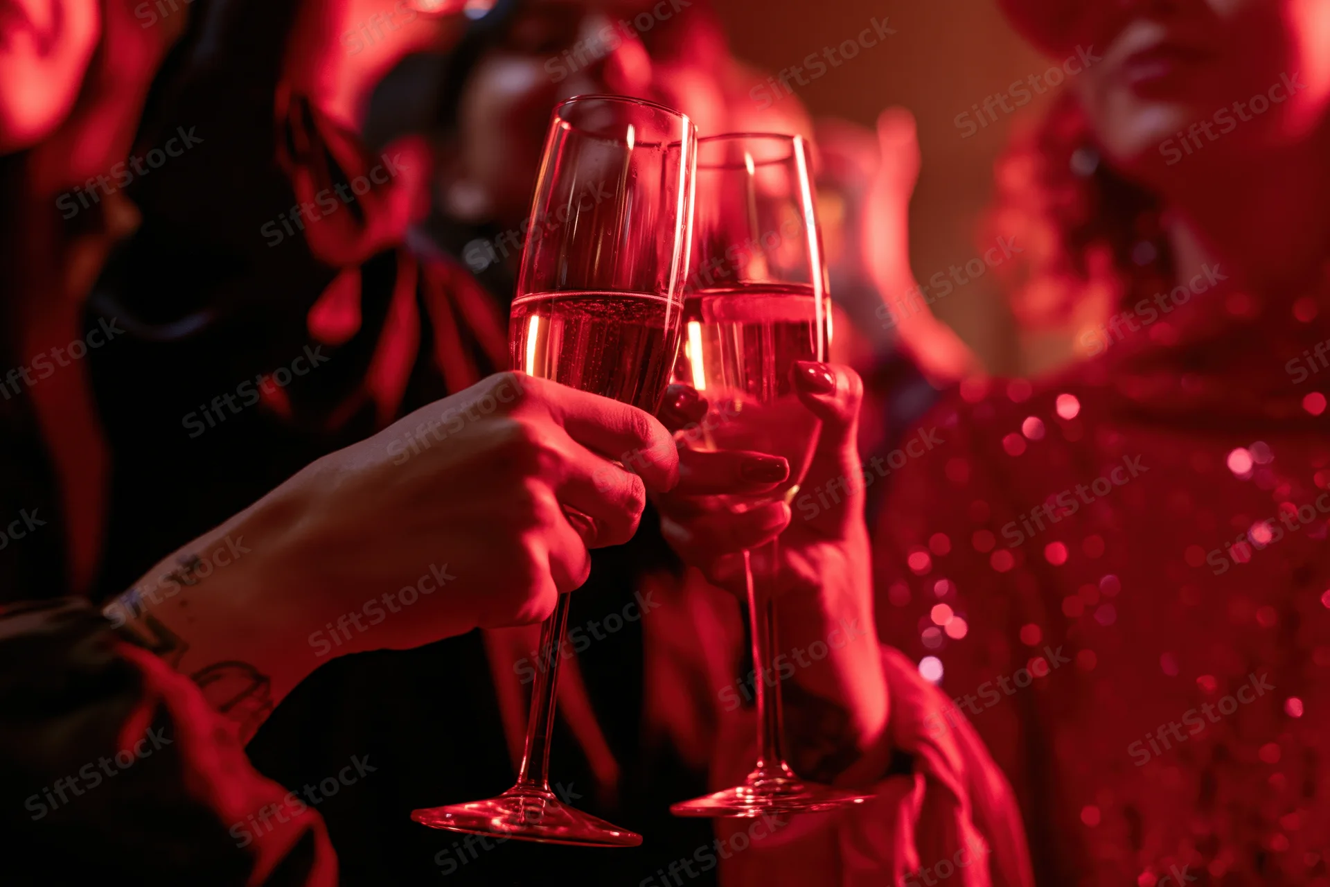 Two women clinking champagne flutes at a festive party under red lighting