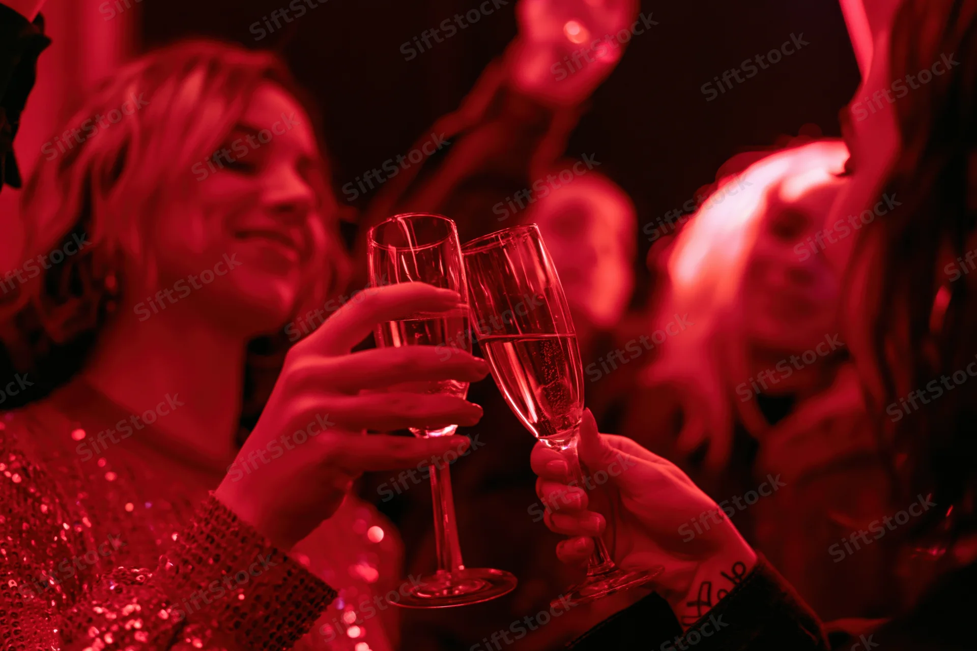 Two women clinking champagne flutes at a festive party under red lighting