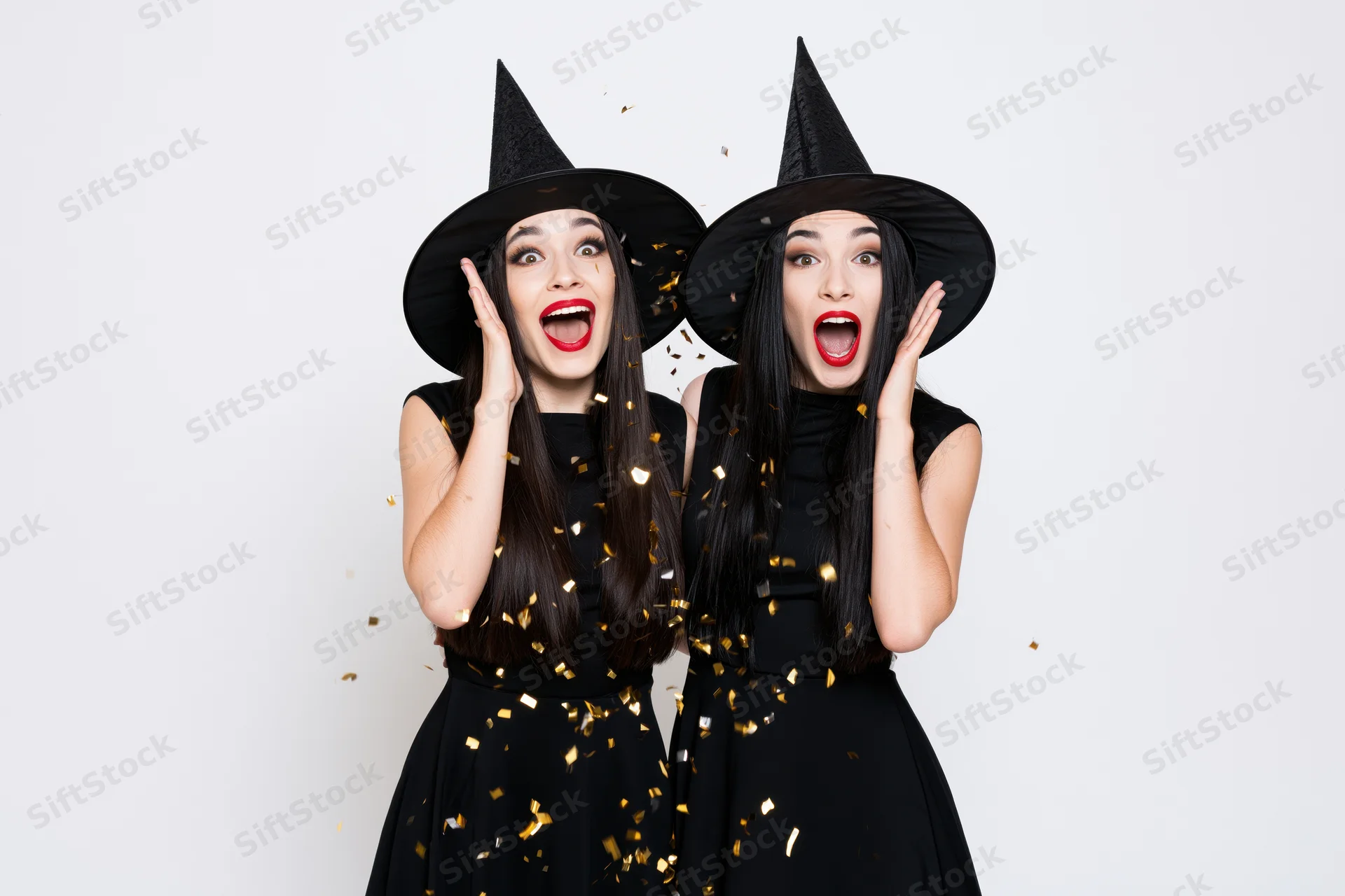 Two young women in witch costumes reacting with surprise amidst falling confetti in a studio setting