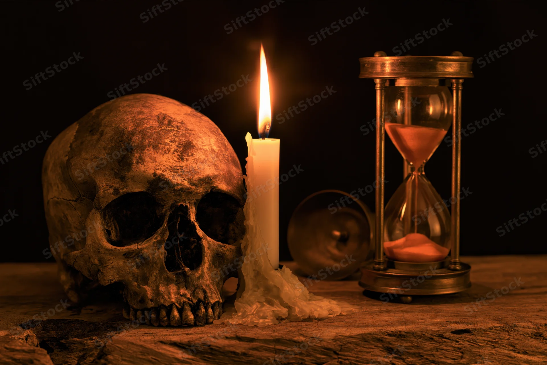 Weathered human skull beside a lit candle and hourglass on a wooden surface