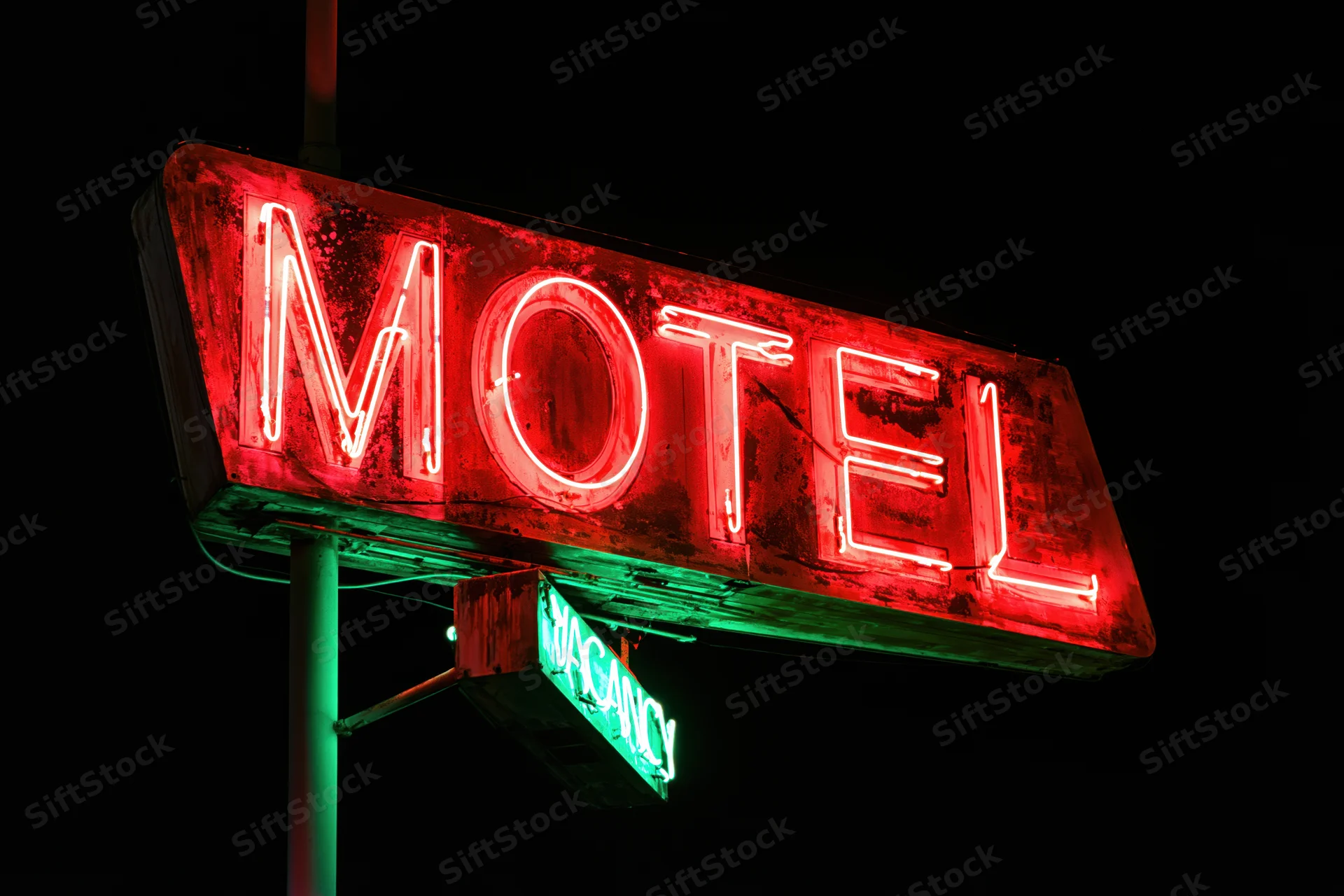 Weathered neon motel sign glowing red at night with green vacancy light below