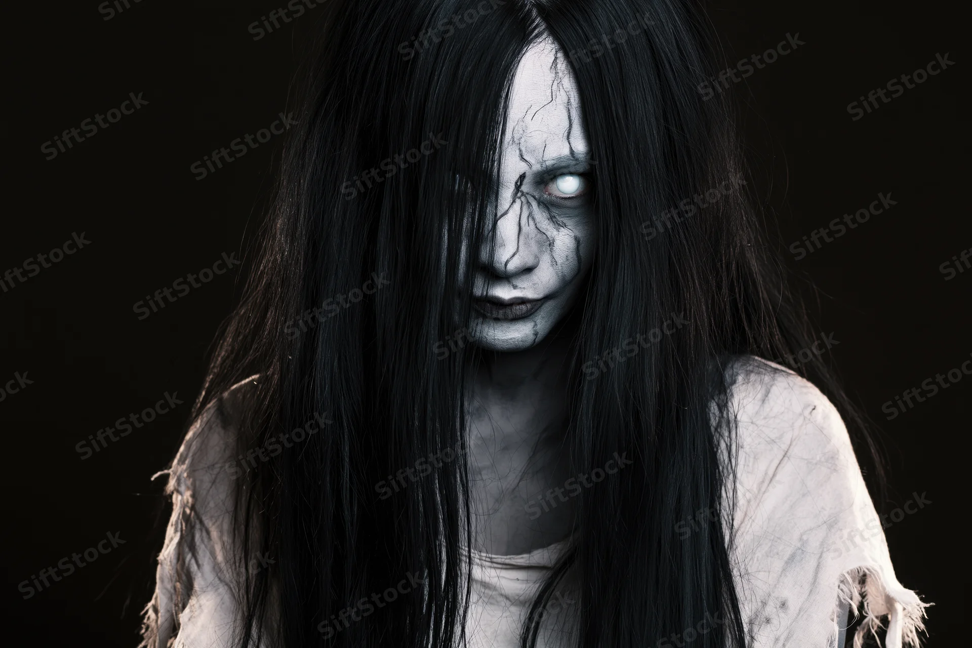 Woman with ghost makeup and long black hair staring intensely in studio portrait