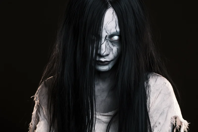 Woman with ghost makeup and long black hair staring intensely in studio portrait
