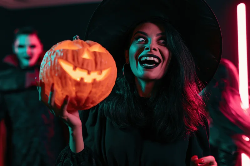 Woman in witch costume holding glowing carved pumpkin at halloween party