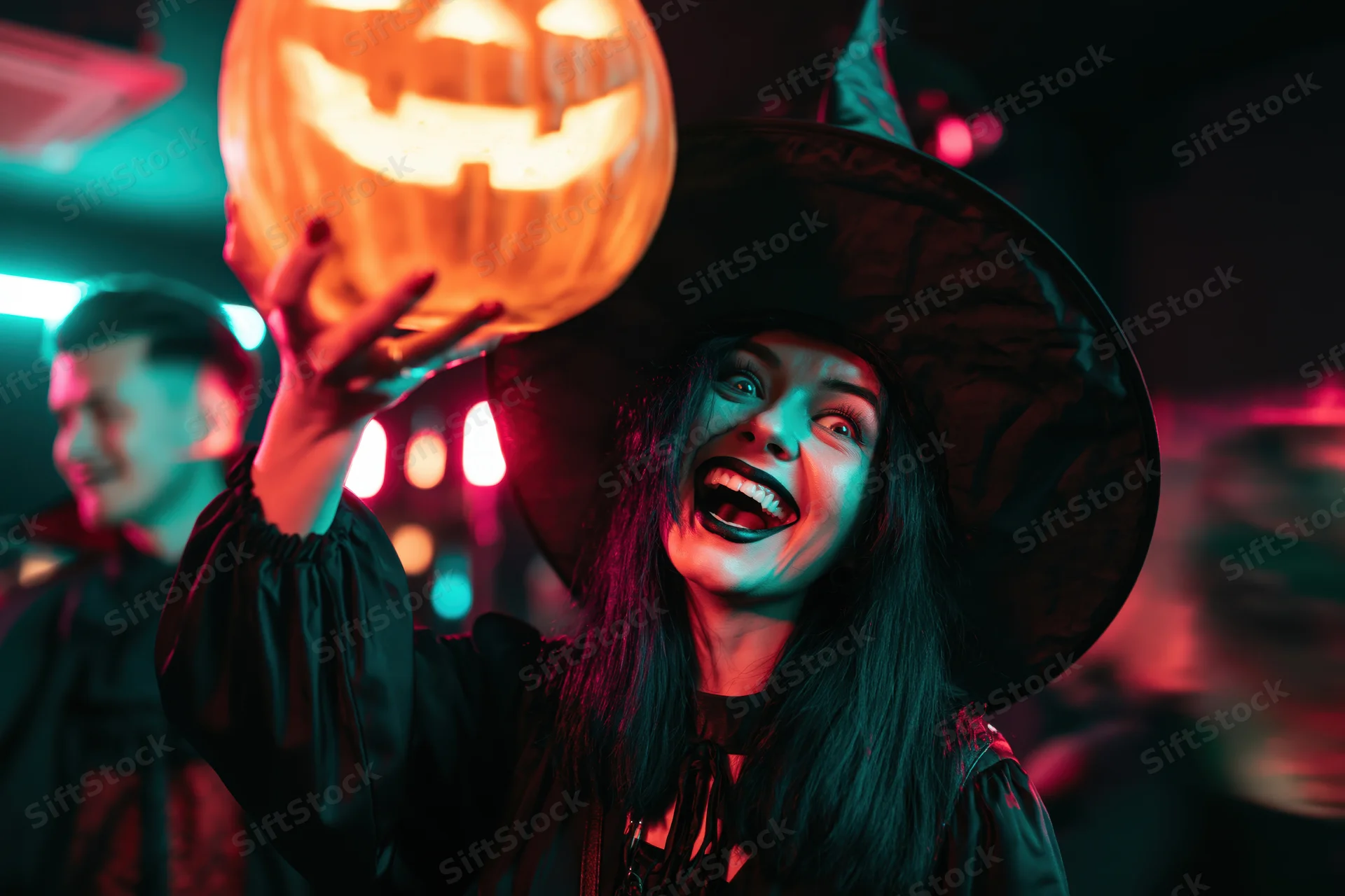 Woman in witch costume holding glowing carved jack-o-lantern at halloween party
