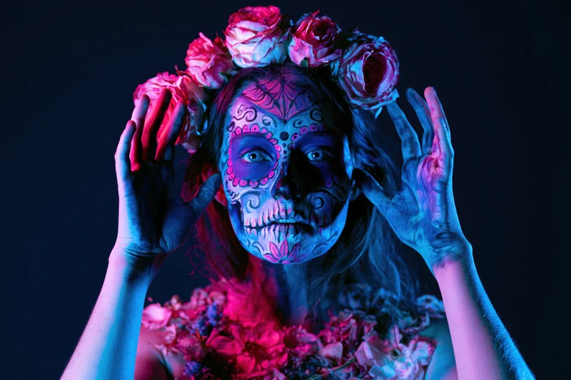 Woman with sugar skull face paint and floral crown under neon lighting in studio